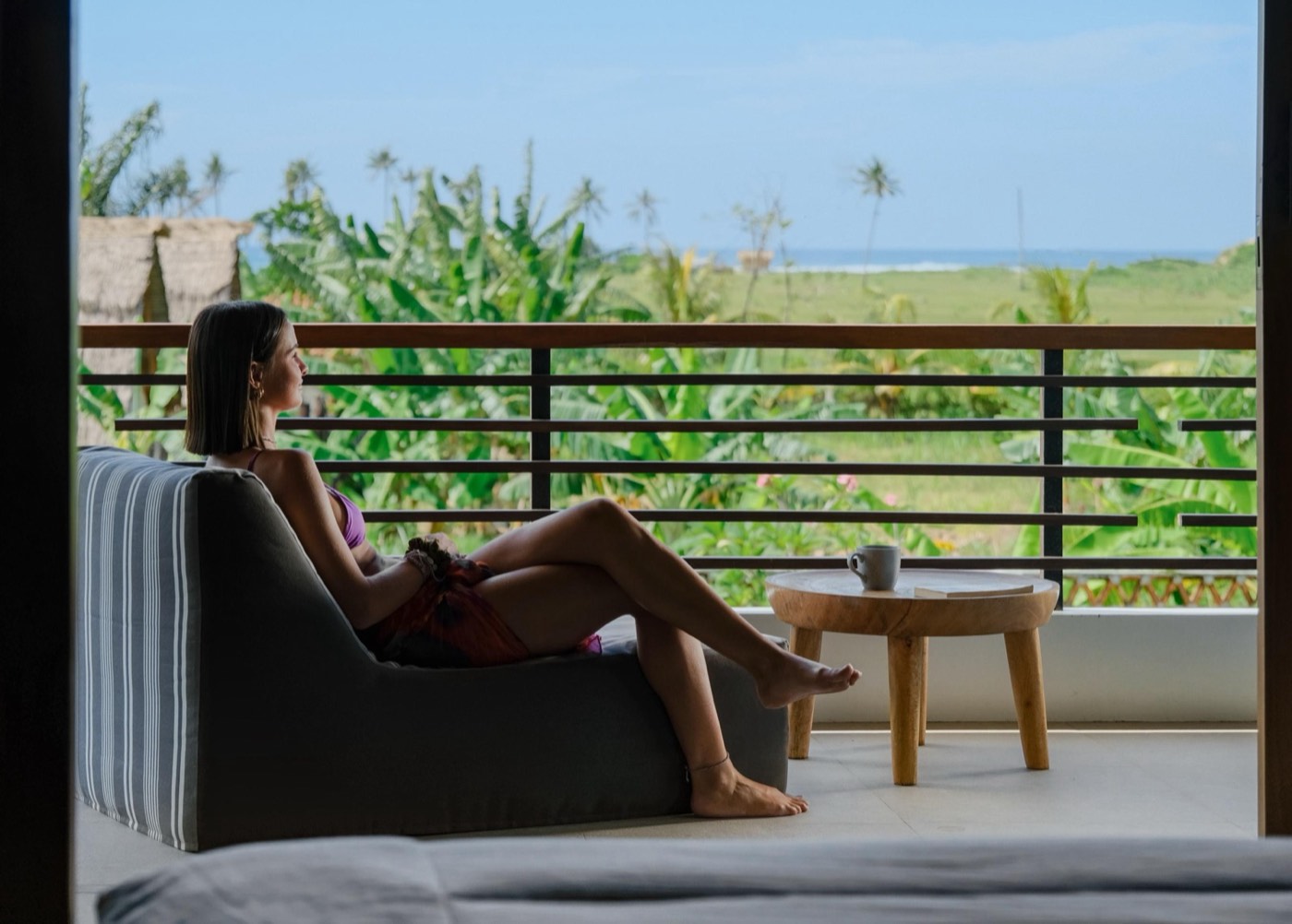 someone sitting on the balcony looking at the sea beyond the palms