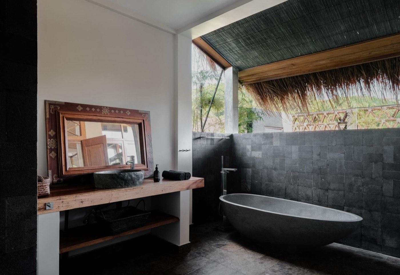 a bathroom with a stone bathtub and a thatched roof outside